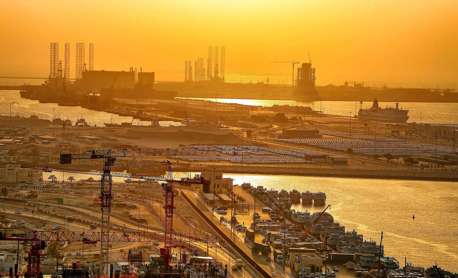 Port Rashid and Dubai's waterfront at sunset, with cranes, roads and moored vessels