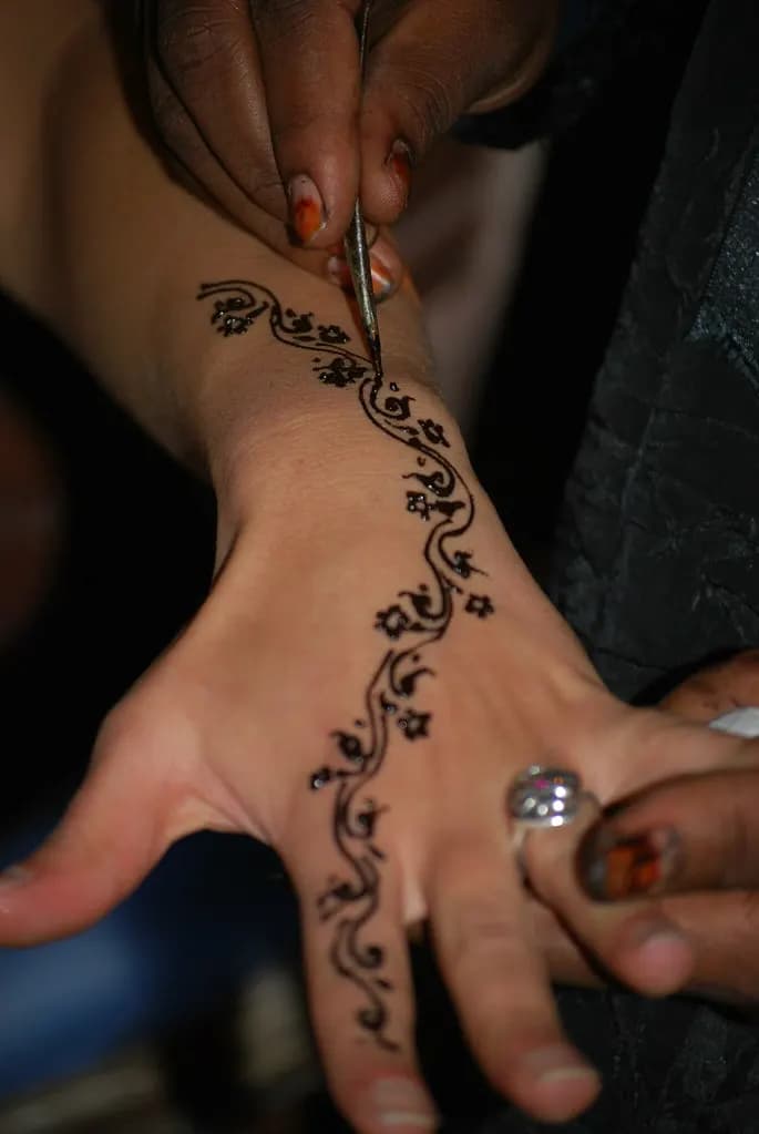 A henna artist drawing a floral design on a client's hand with a fine cone