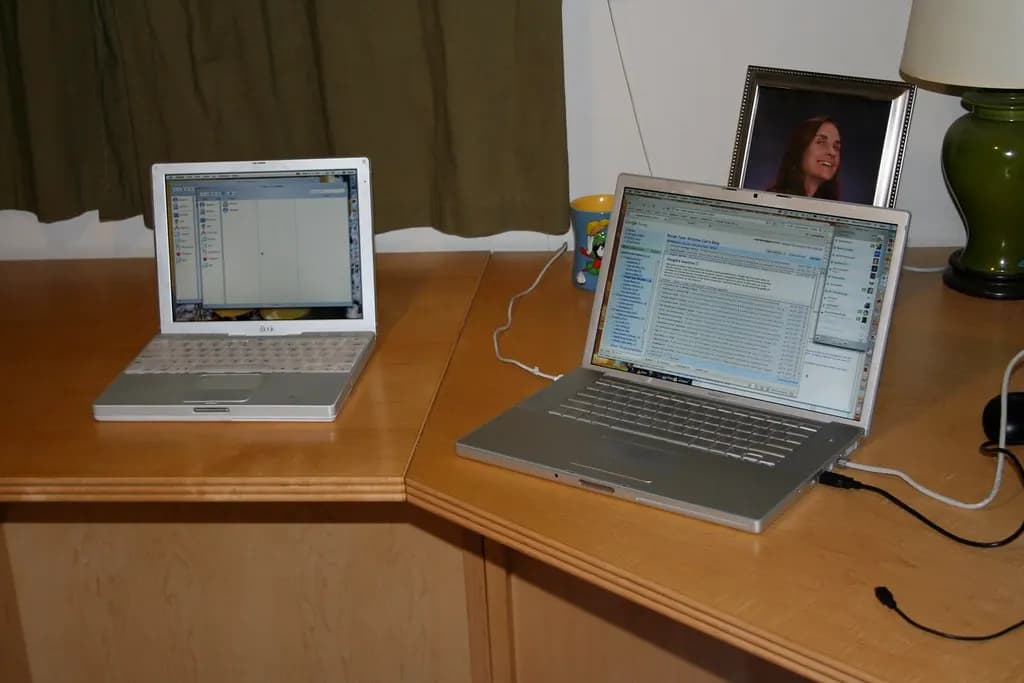 Two laptops set up on a wooden desk at home