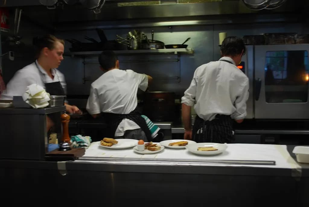 Chefs preparing dishes at the pass of an open restaurant kitchen with stainless steel counters