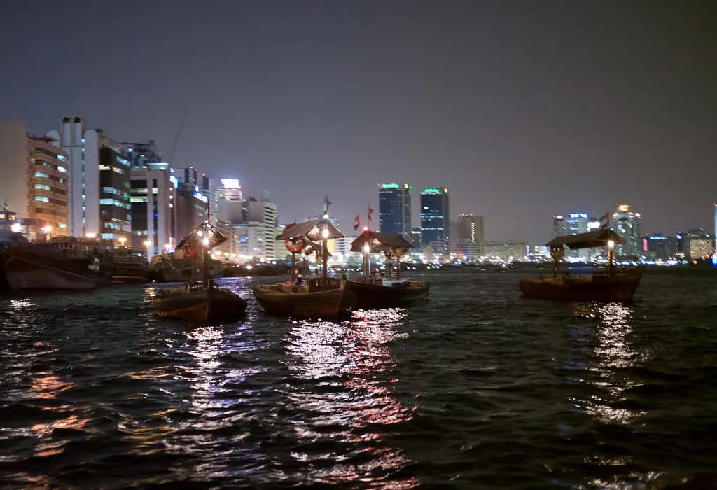 Wooden abra boats moored on Dubai Creek at night with the Deira skyline behind