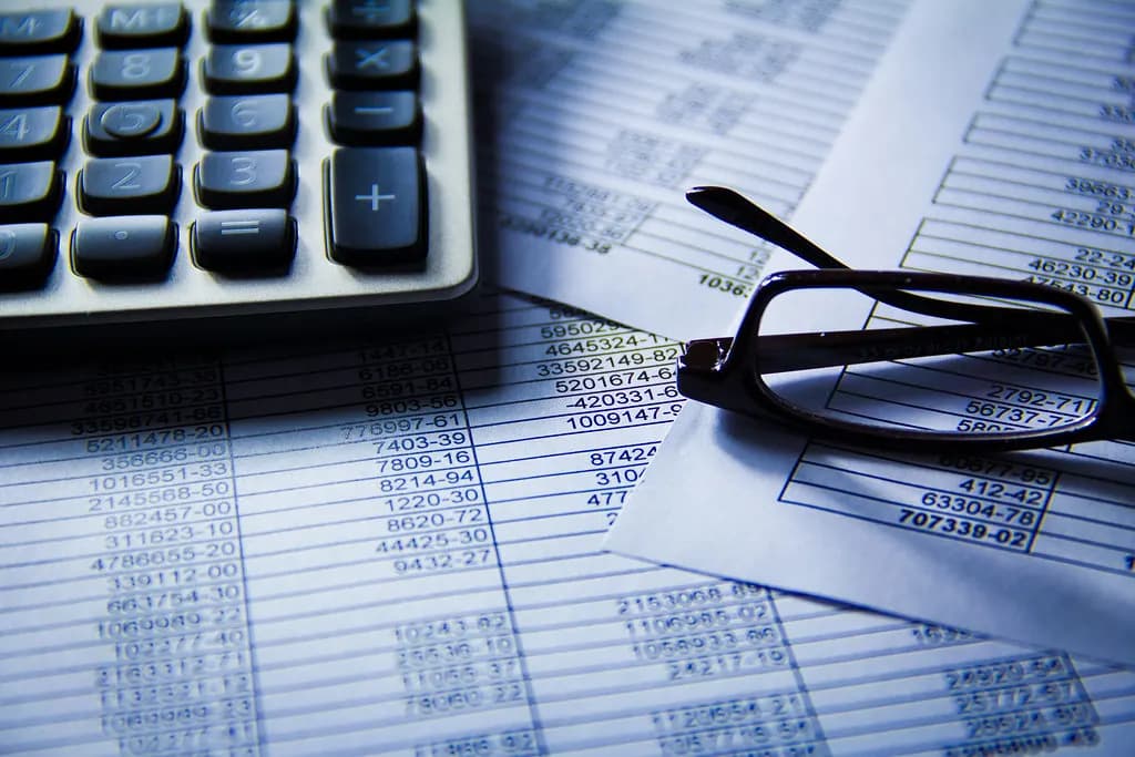 A calculator and reading glasses on printed financial spreadsheets