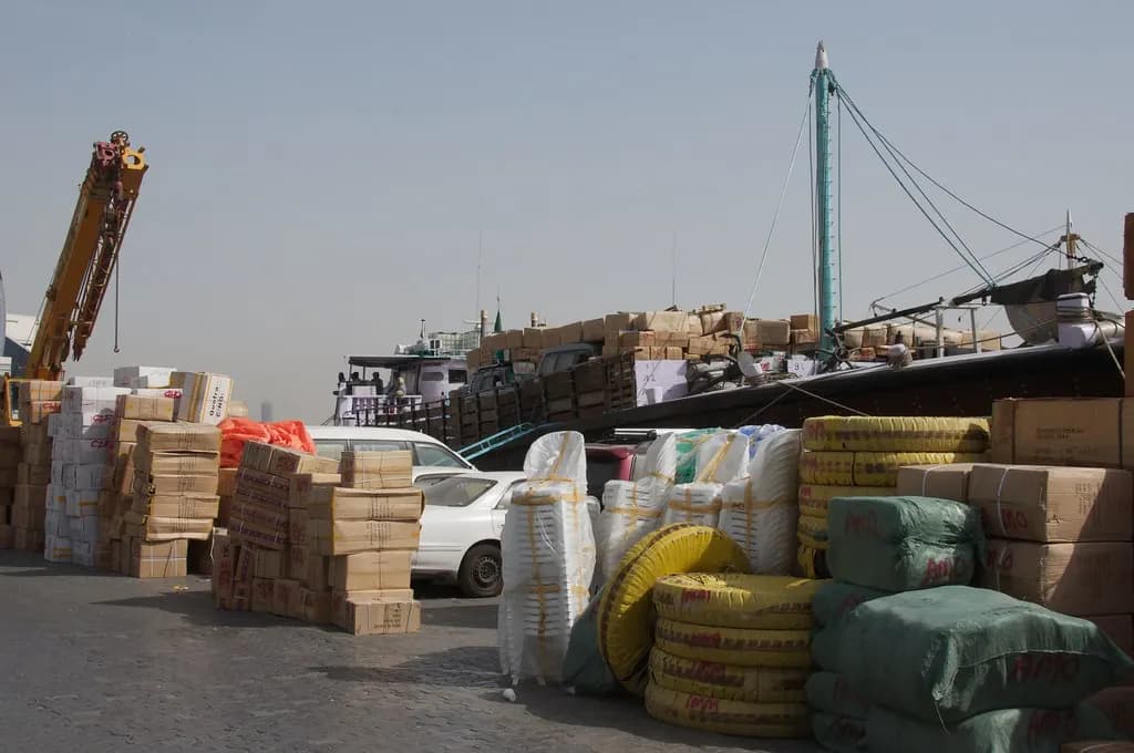 Cartons and bales of cargo stacked on the wharf beside a dhow at Dubai Creek