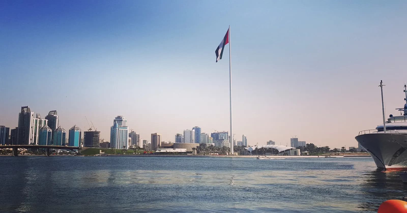 View across the water to Sharjah's waterfront and port area with a tall flagpole