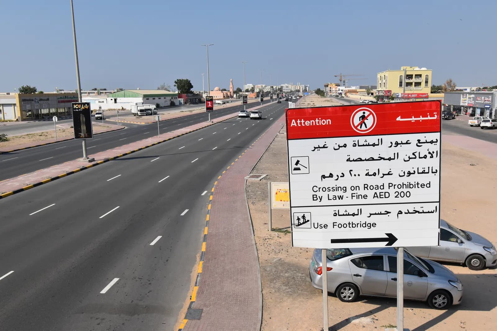 King Faisal Road in Umm Al Quwain with low-rise shops and buildings and a pedestrian safety sign