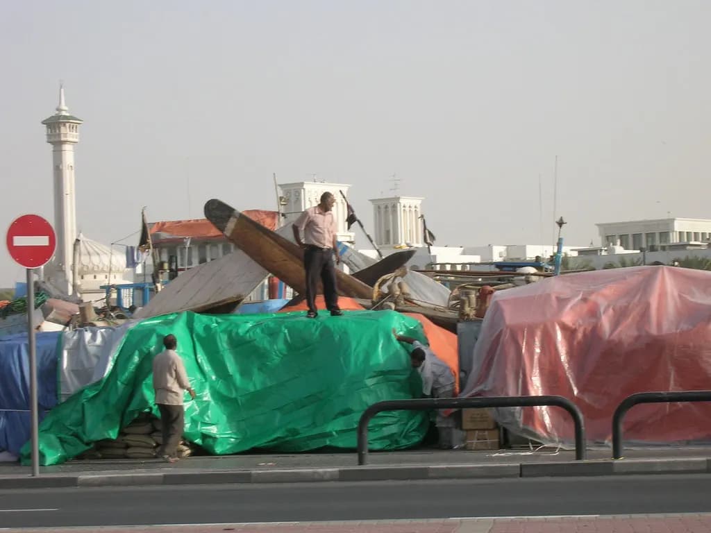 Bundled cargo stacked on the wharf beside dhows at Dubai Creek