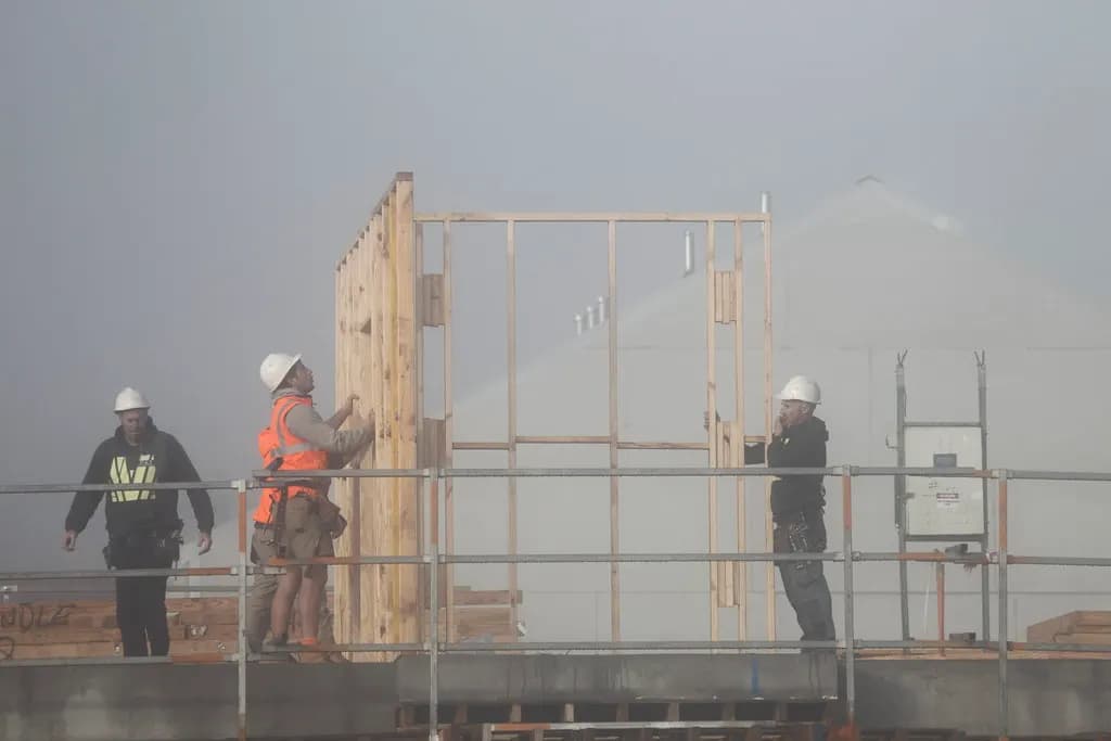 Builders in hard hats and high-visibility vests putting up a timber frame on an elevated deck