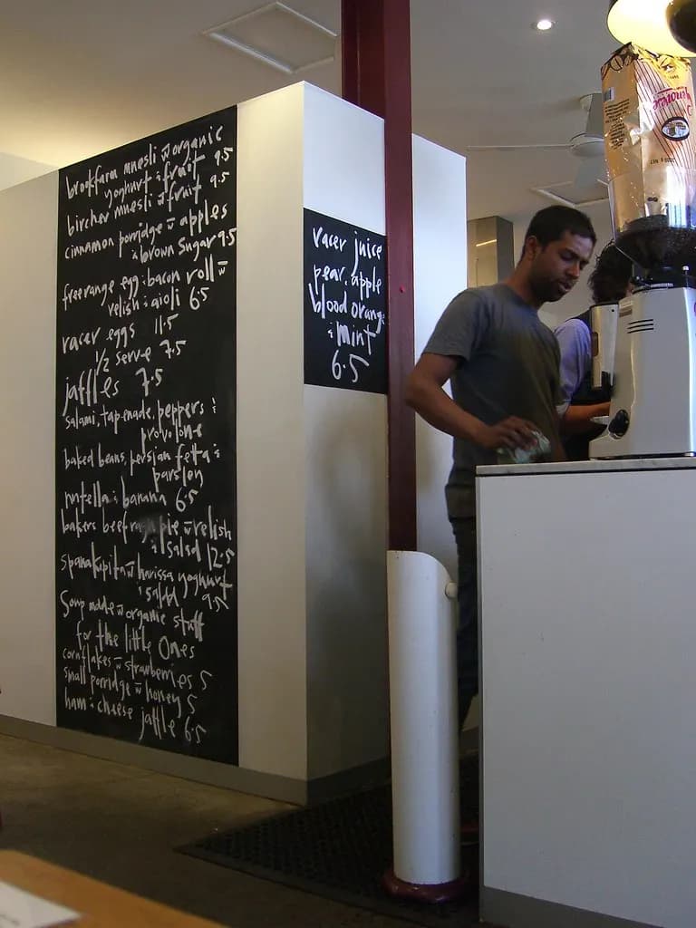 Barista working behind the counter under a chalk blackboard menu in a Melbourne cafe