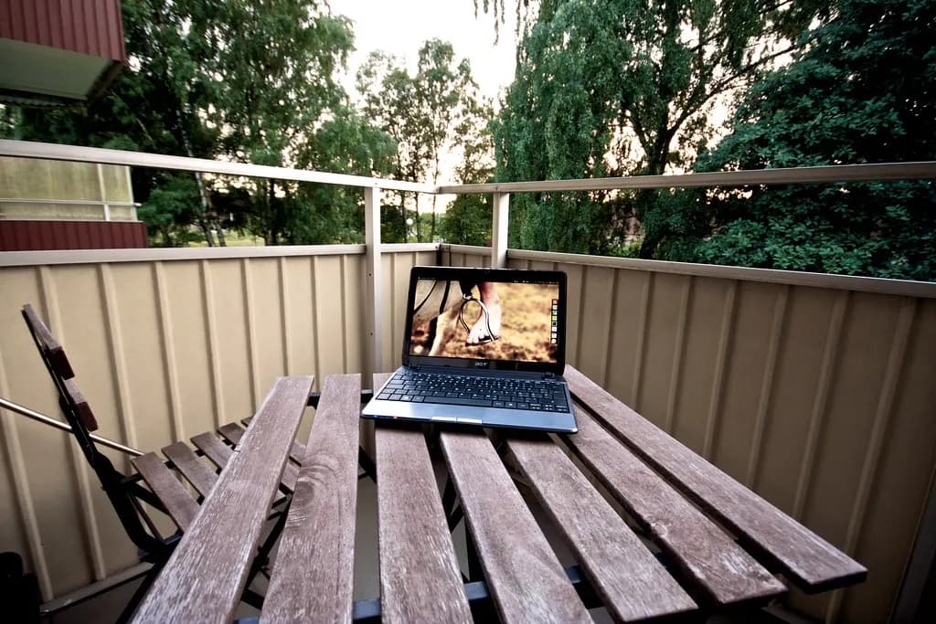 A laptop on a wooden table on a balcony, set up for working from home