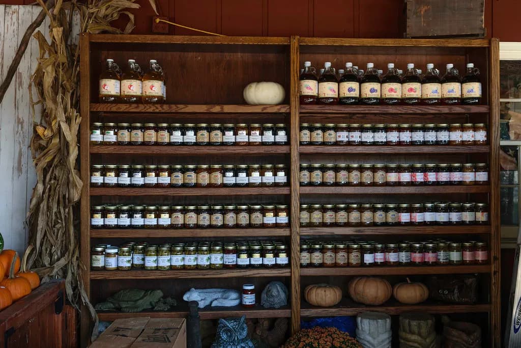 Wooden shelves stacked with labelled jars of jams and preserves at a farmers market stall