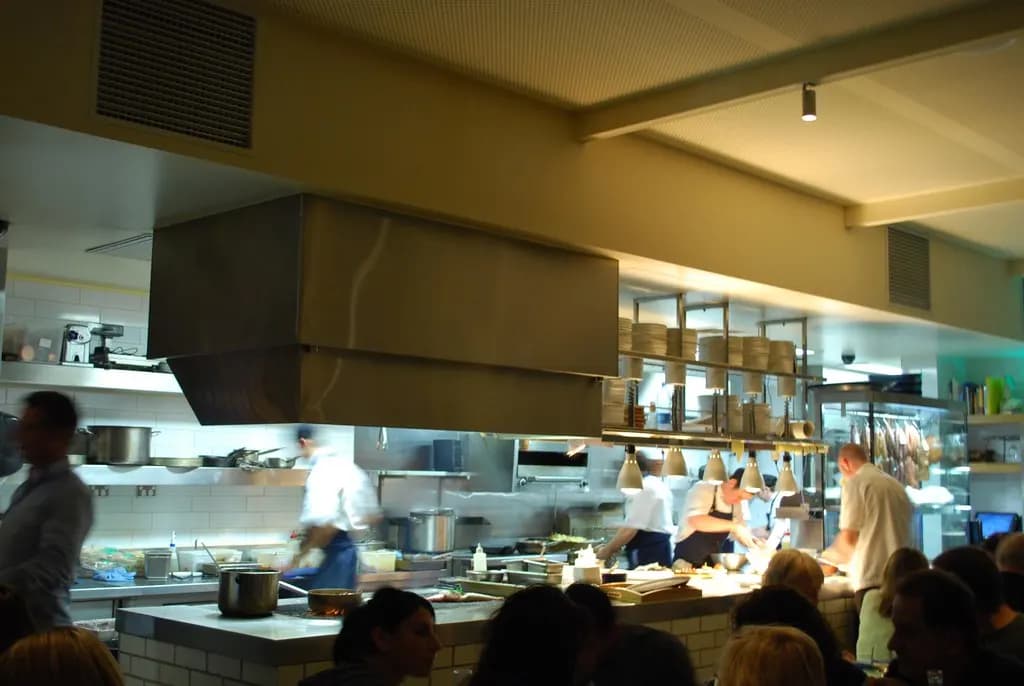 Chefs working in a busy open restaurant kitchen at night with diners at the counter