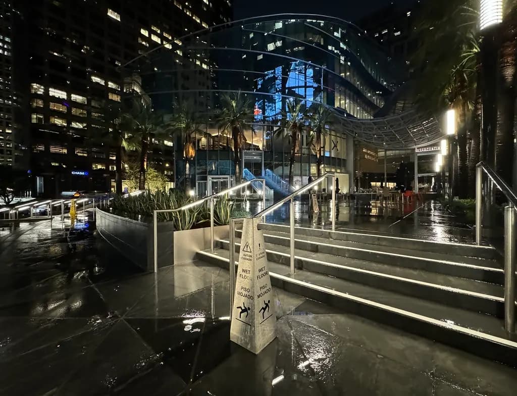 Yellow wet floor caution sign on rain-soaked steps outside a city office plaza at night