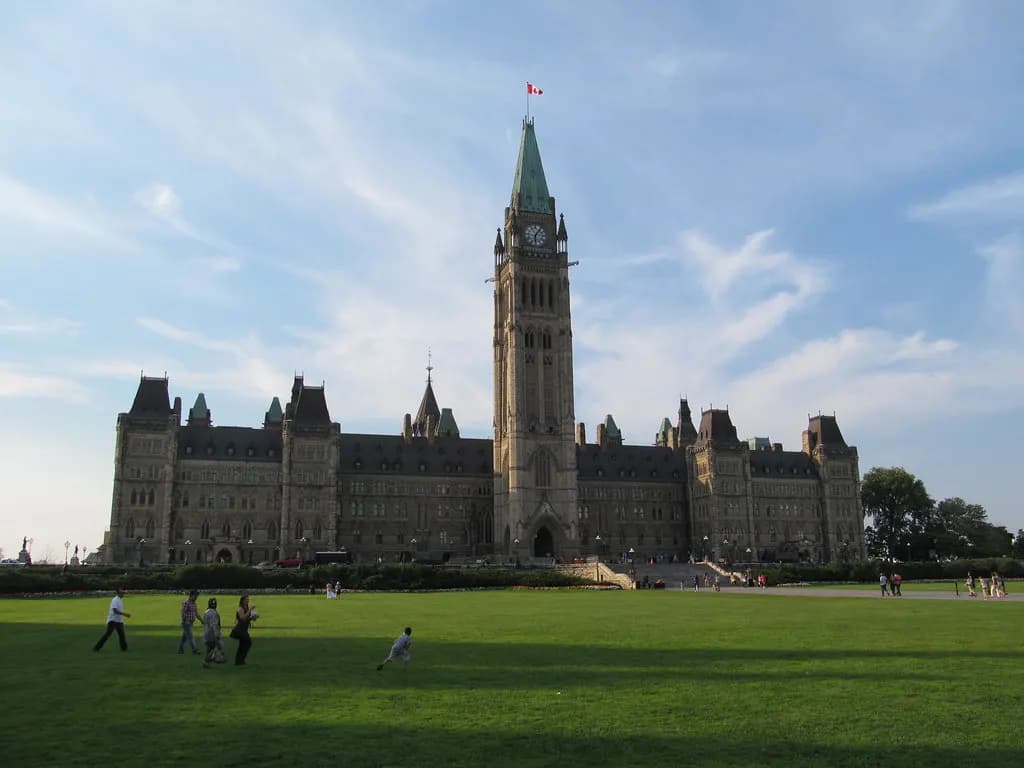 Centre Block and Peace Tower on Parliament Hill in Ottawa on a summer evening, with people on the lawn