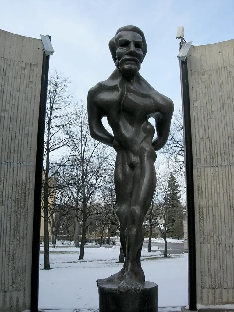 A modernist bronze sculpture of Louis Riel standing between two curved concrete walls in winter, in Saint-Boniface, Winnipeg