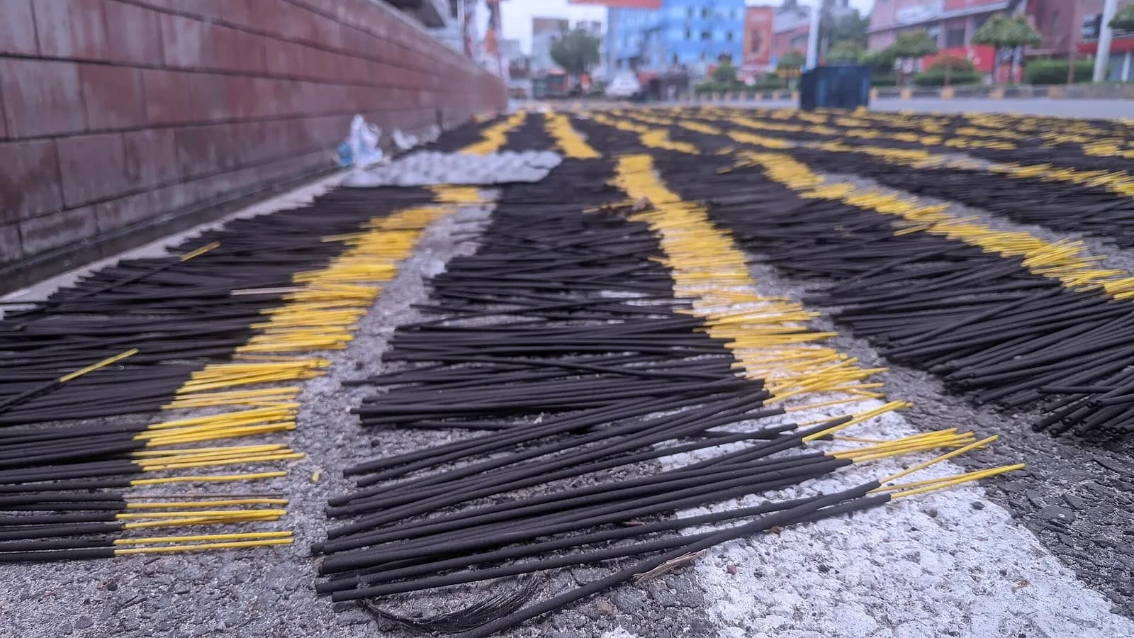 Rows of freshly rolled black raw incense sticks with yellow bamboo ends laid out to dry on a paved roadside