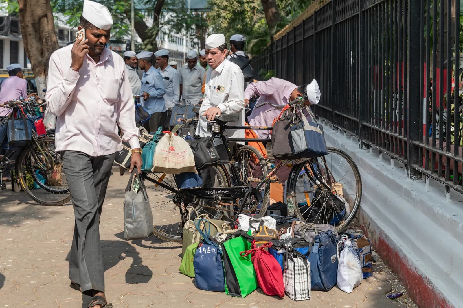 Dabbawalas sorting home-cooked tiffin bags next to bicycles on a Mumbai street