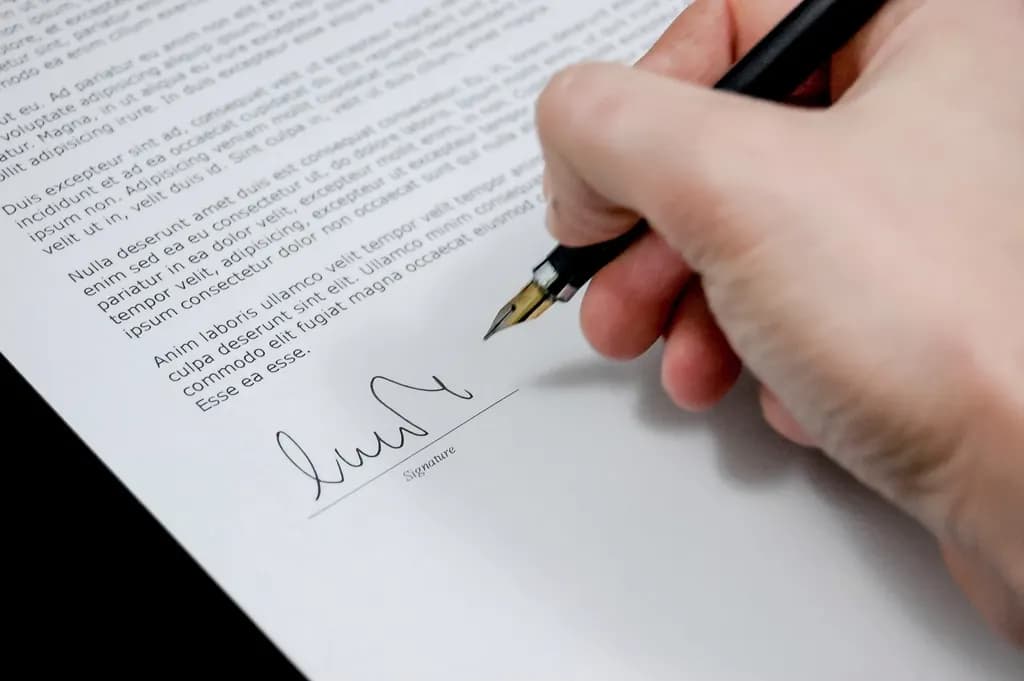 A hand holding a pen signing a printed document