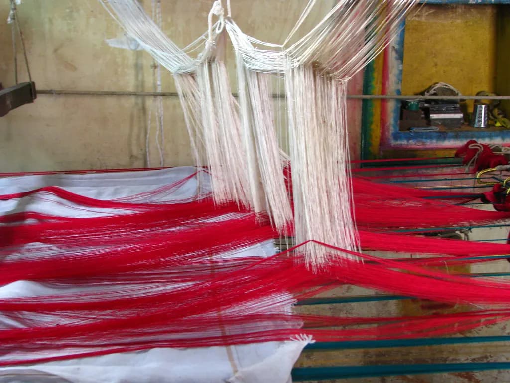 Red and white silk warp threads stretched across a handloom in a Kanchipuram weaving workshop