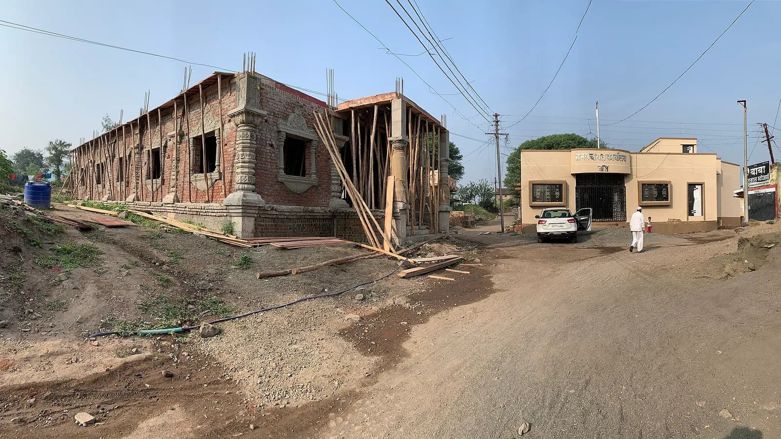 A brick building under construction beside a road in India, with RCC columns and timber scaffolding