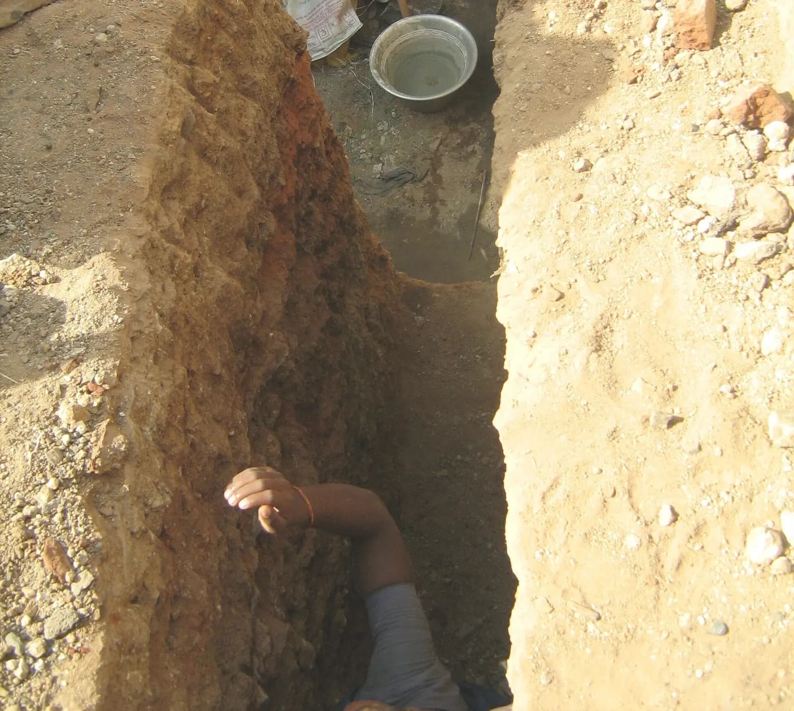 A freshly dug foundation trench for a house in Tamil Nadu, with a worker measuring its depth