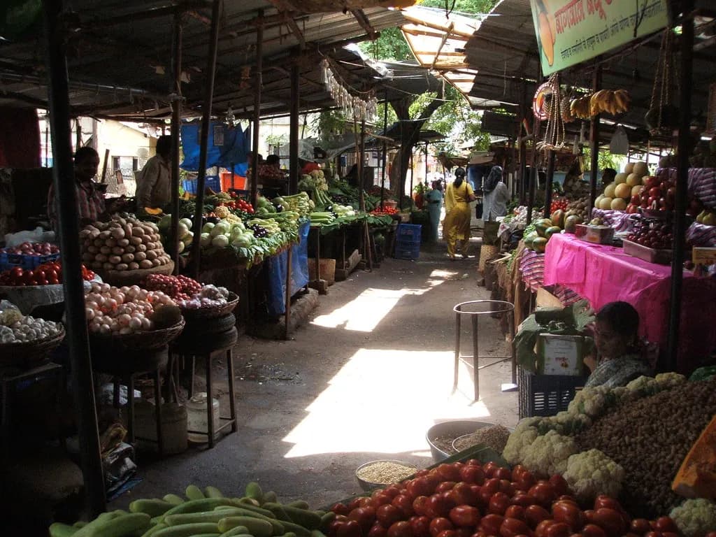 Covered vegetable market in India with stalls of tomatoes, cauliflower, potatoes, onions and fruit