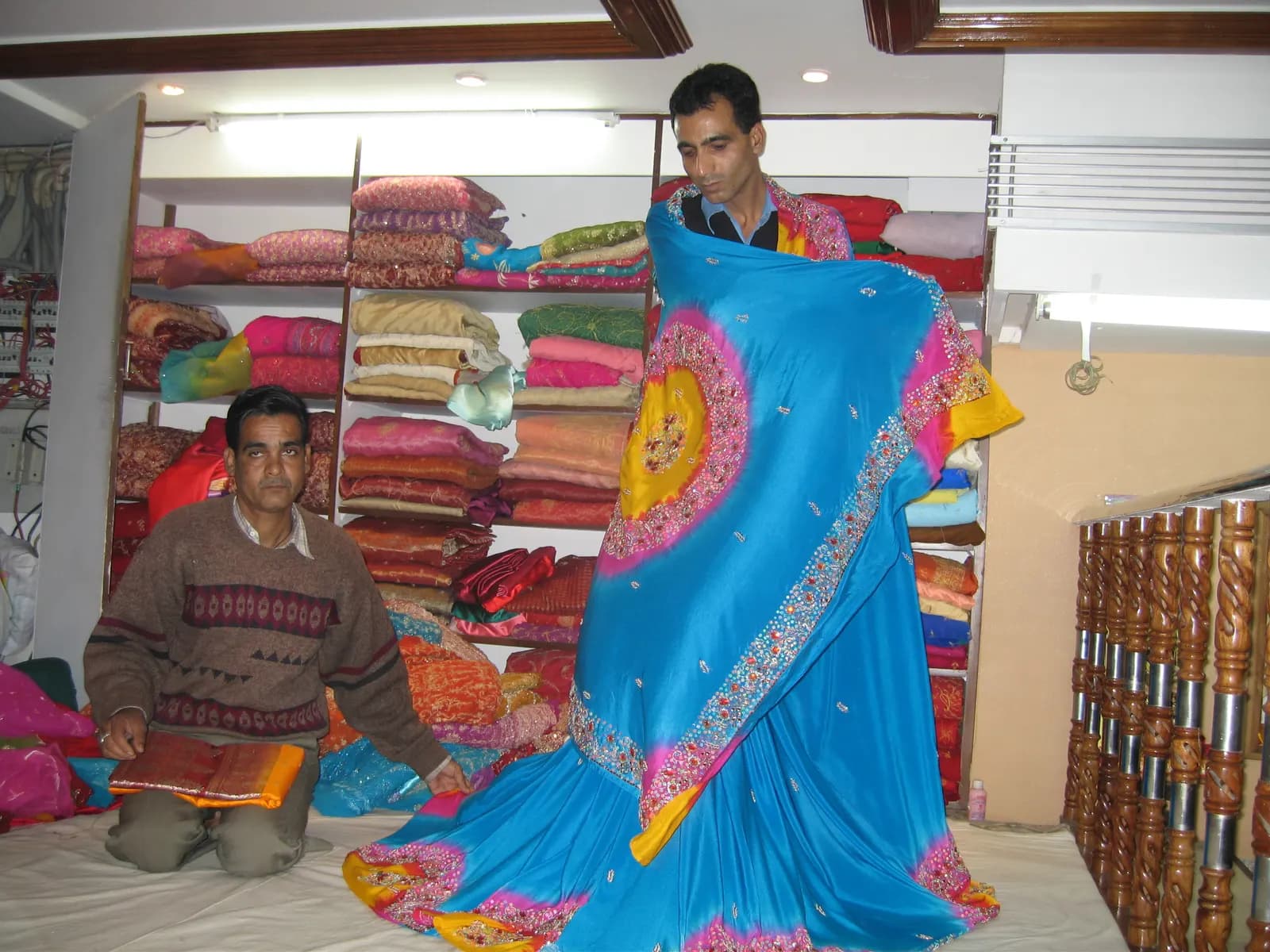 A shop assistant holds up a blue embroidered lehenga in front of shelves of folded festive wear