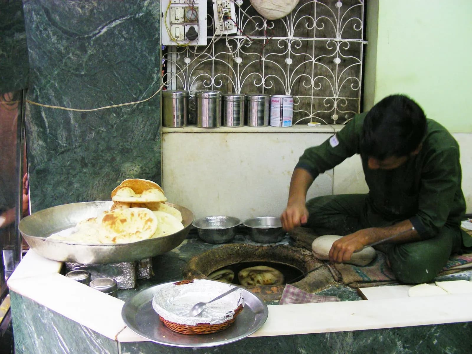 A cook making naan at a tandoor in a restaurant kitchen in Delhi