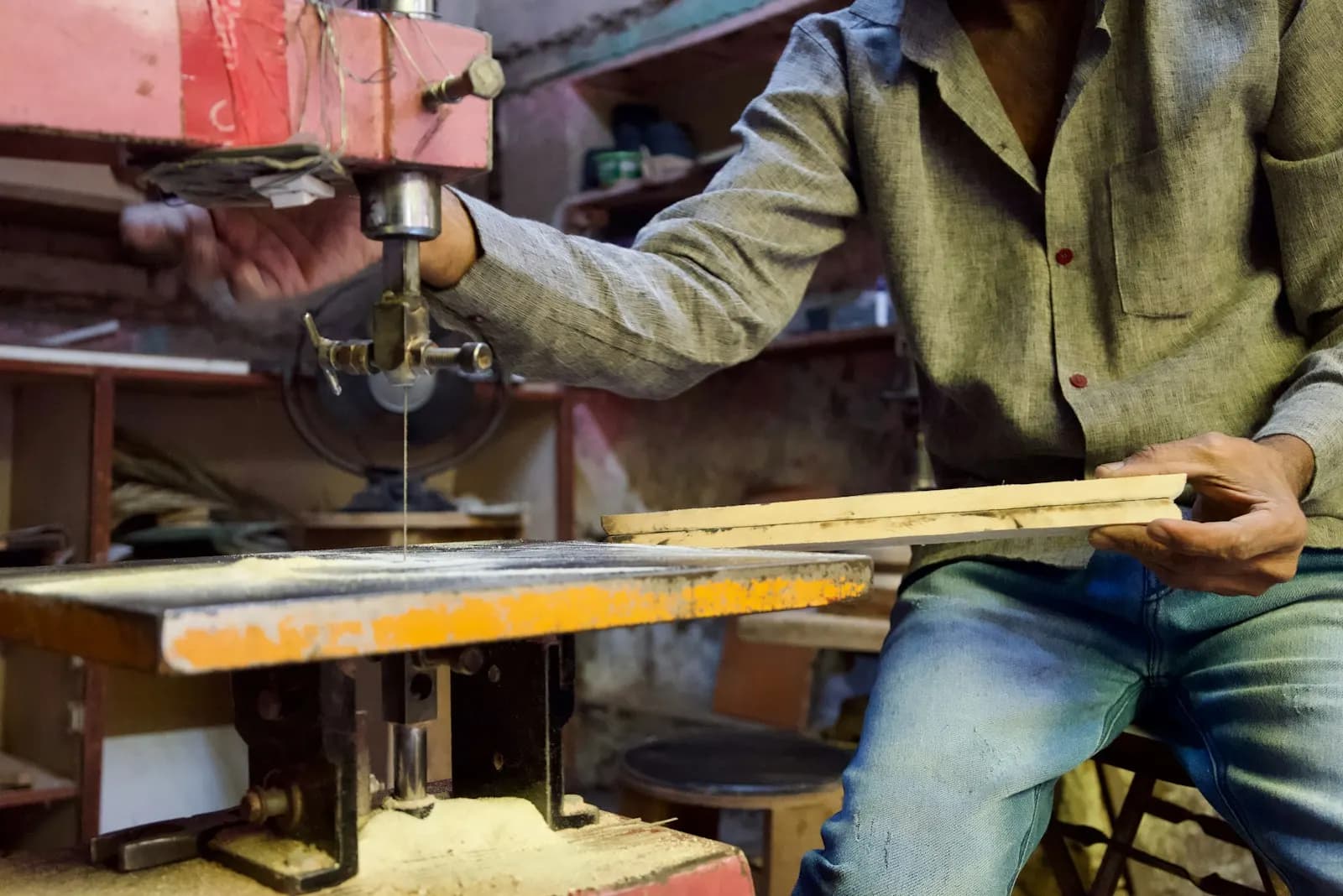 A carpenter cutting a plank on a band saw in a small workshop