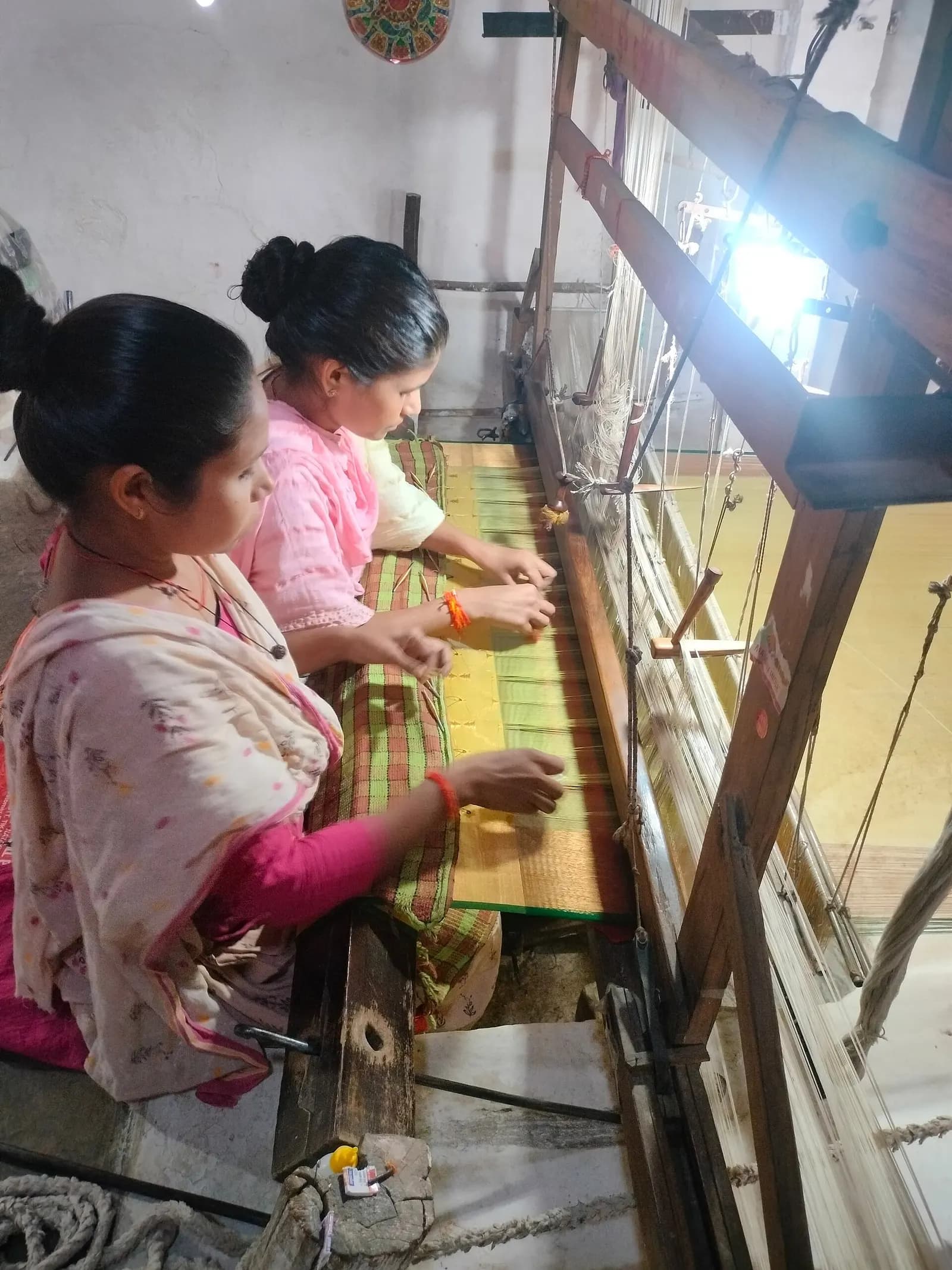 Two women weaving cloth on a wooden handloom in India