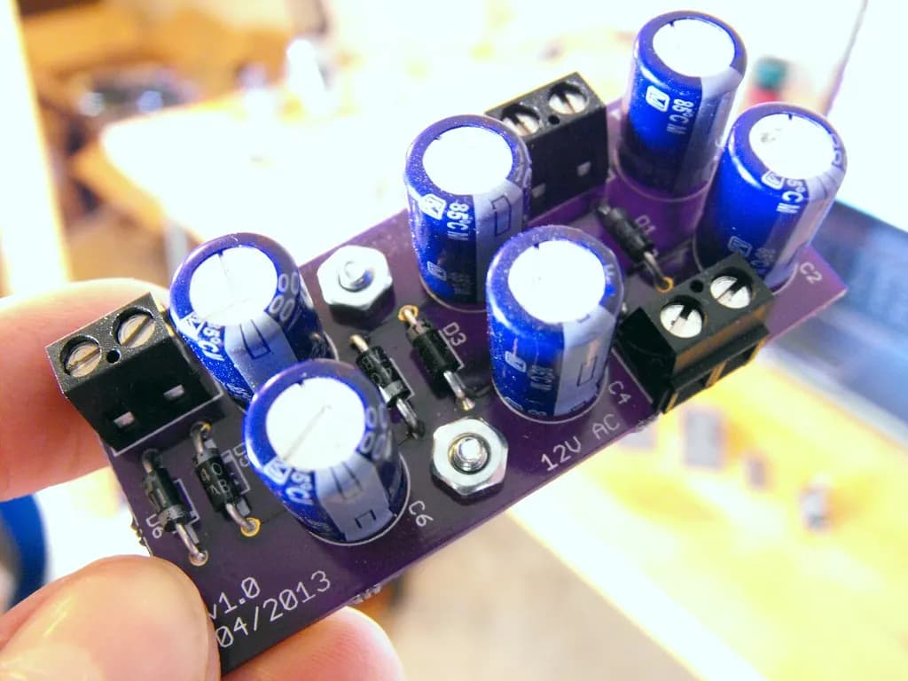 A hand holding a small custom-made printed circuit board with capacitors and terminal blocks