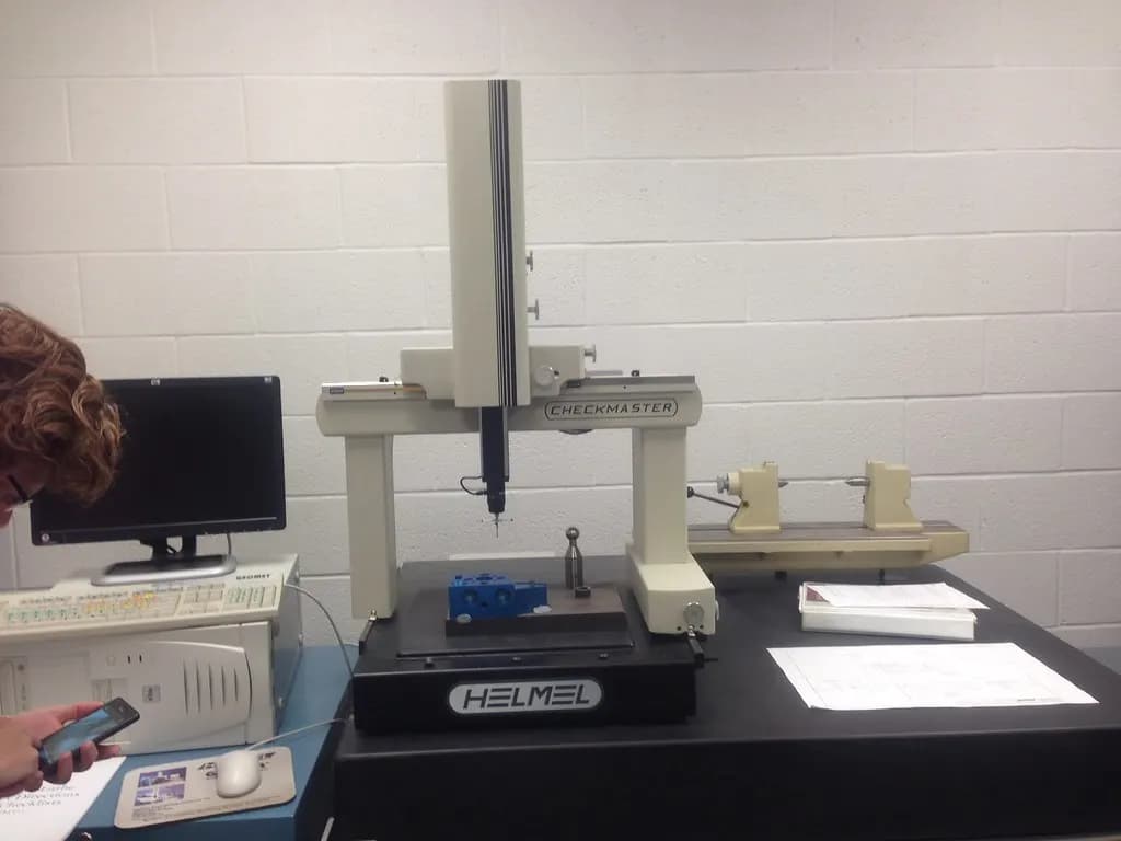 A bridge-type coordinate measuring machine with a touch probe inspecting a small blue part in a metrology lab