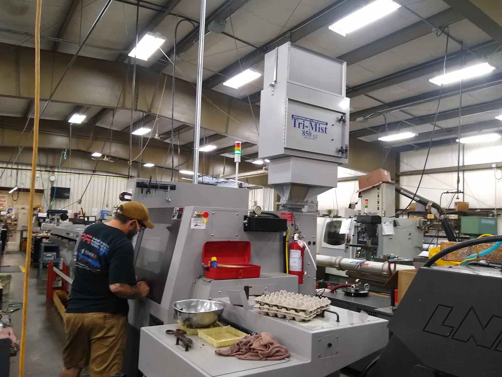 An operator loading a Tsugami CNC lathe with a bar feeder on a busy machine-shop floor