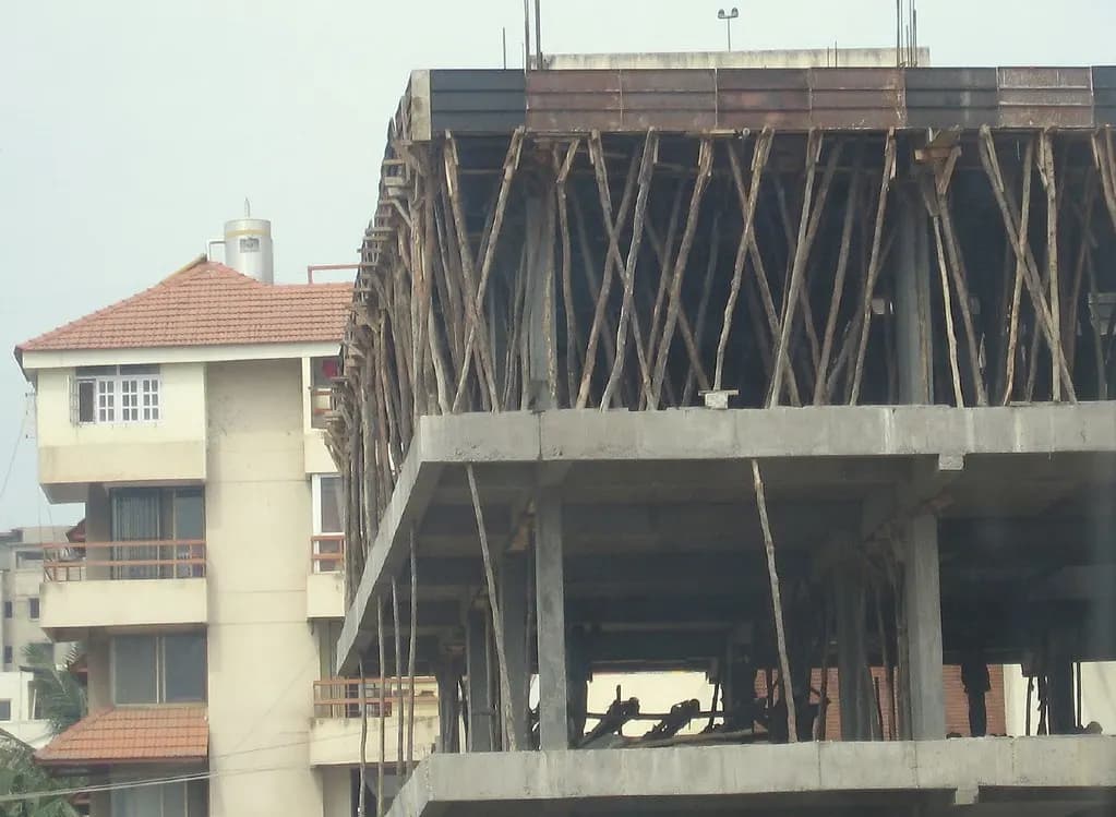 A multi-storey concrete building under construction in Bangalore, with wooden props and scaffolding supporting the upper slab