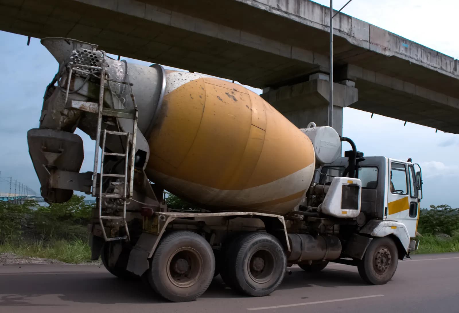 A ready-mix concrete transit mixer truck parked on a road beside an elevated highway in Kerala