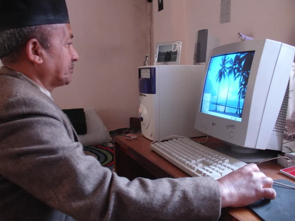 A man in a traditional cap working on a desktop computer in a small office