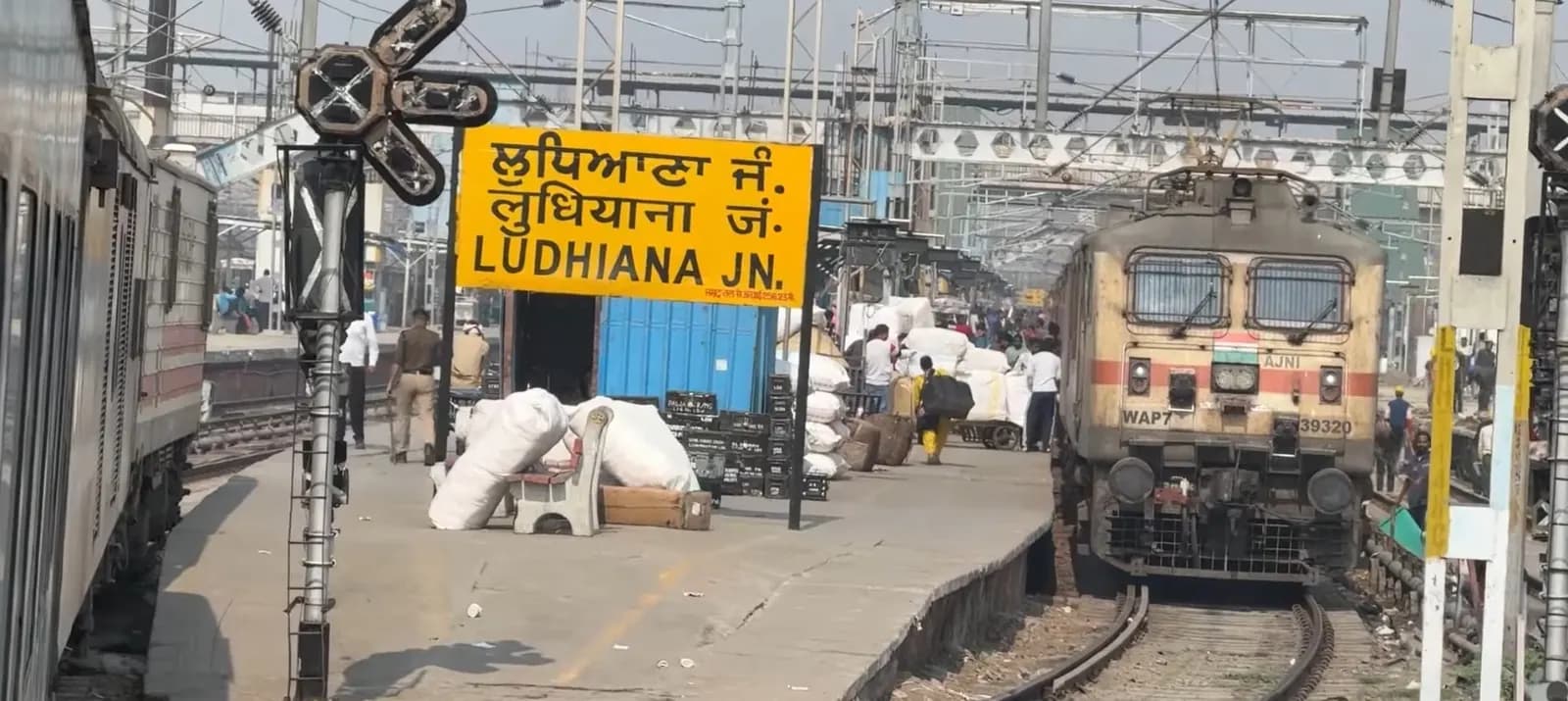 Platform at Ludhiana Junction railway station with the yellow station sign in Punjabi, Hindi and English and an electric locomotive