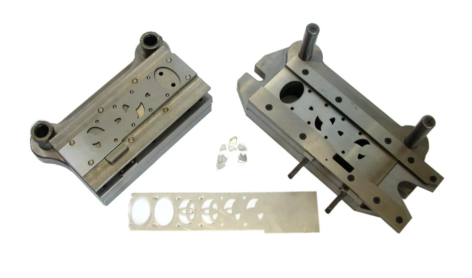 A two-part progressive press die opened up, with the punched steel strip and scrap pieces showing each stamping stage