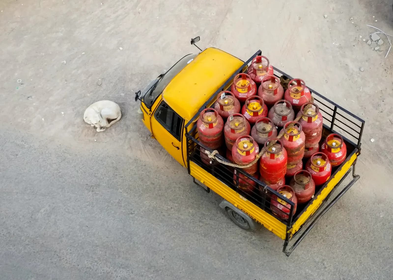 Three-wheeler goods carrier loaded with red LPG cylinders, seen from above on a Hyderabad street