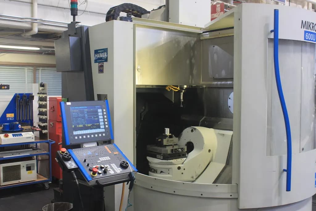 A CNC milling machine with its door open and the control panel beside it on a workshop floor