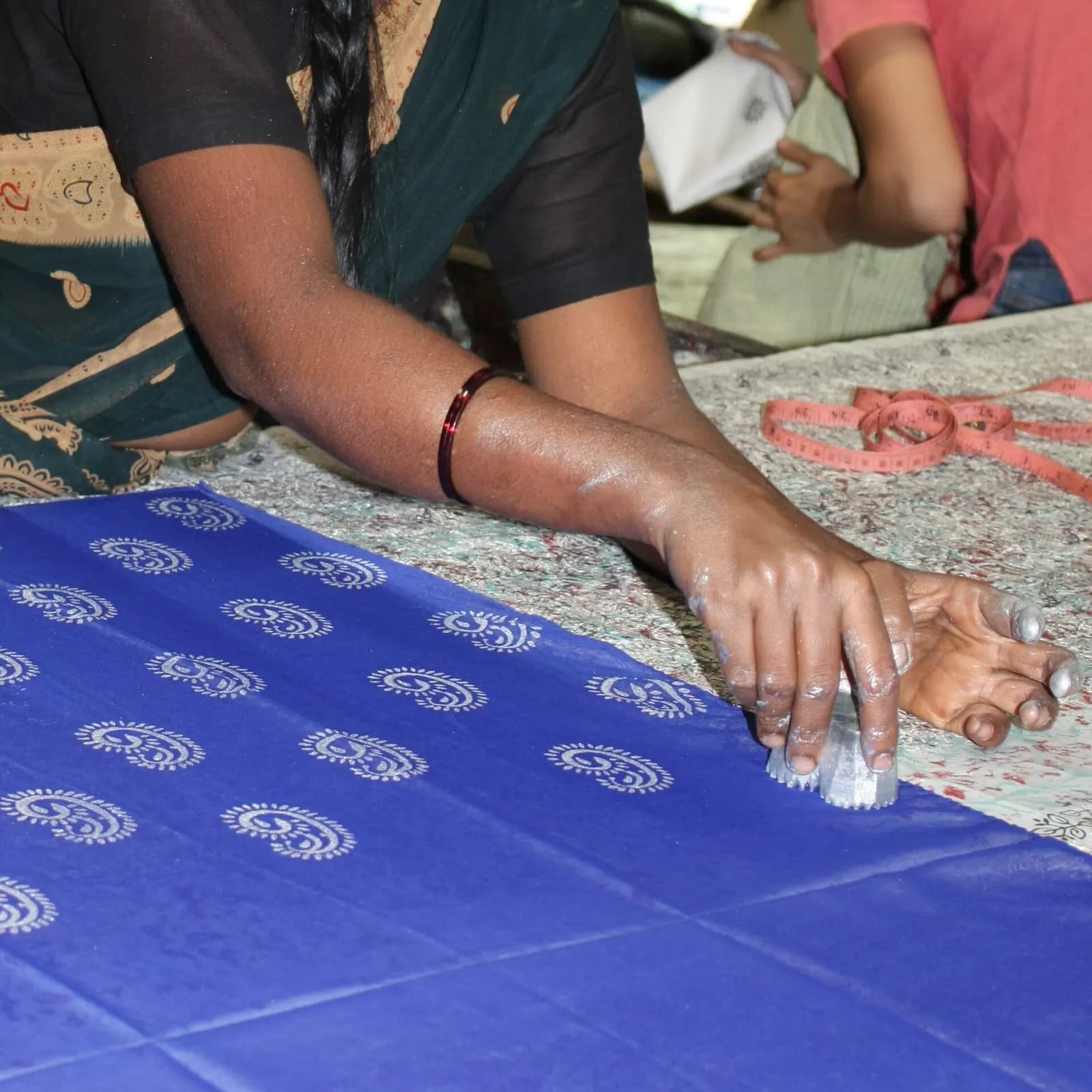 A worker hand block-printing a white paisley motif in rows on blue fabric in Halasur village, Karnataka