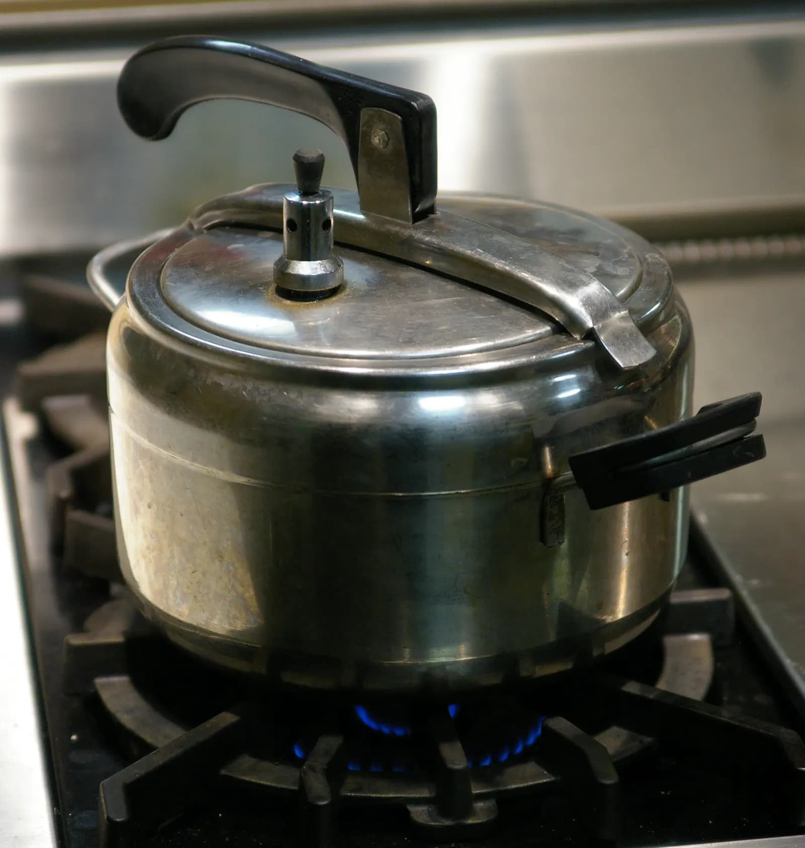A stainless steel pressure cooker with an oval lid and black handles on a gas stove