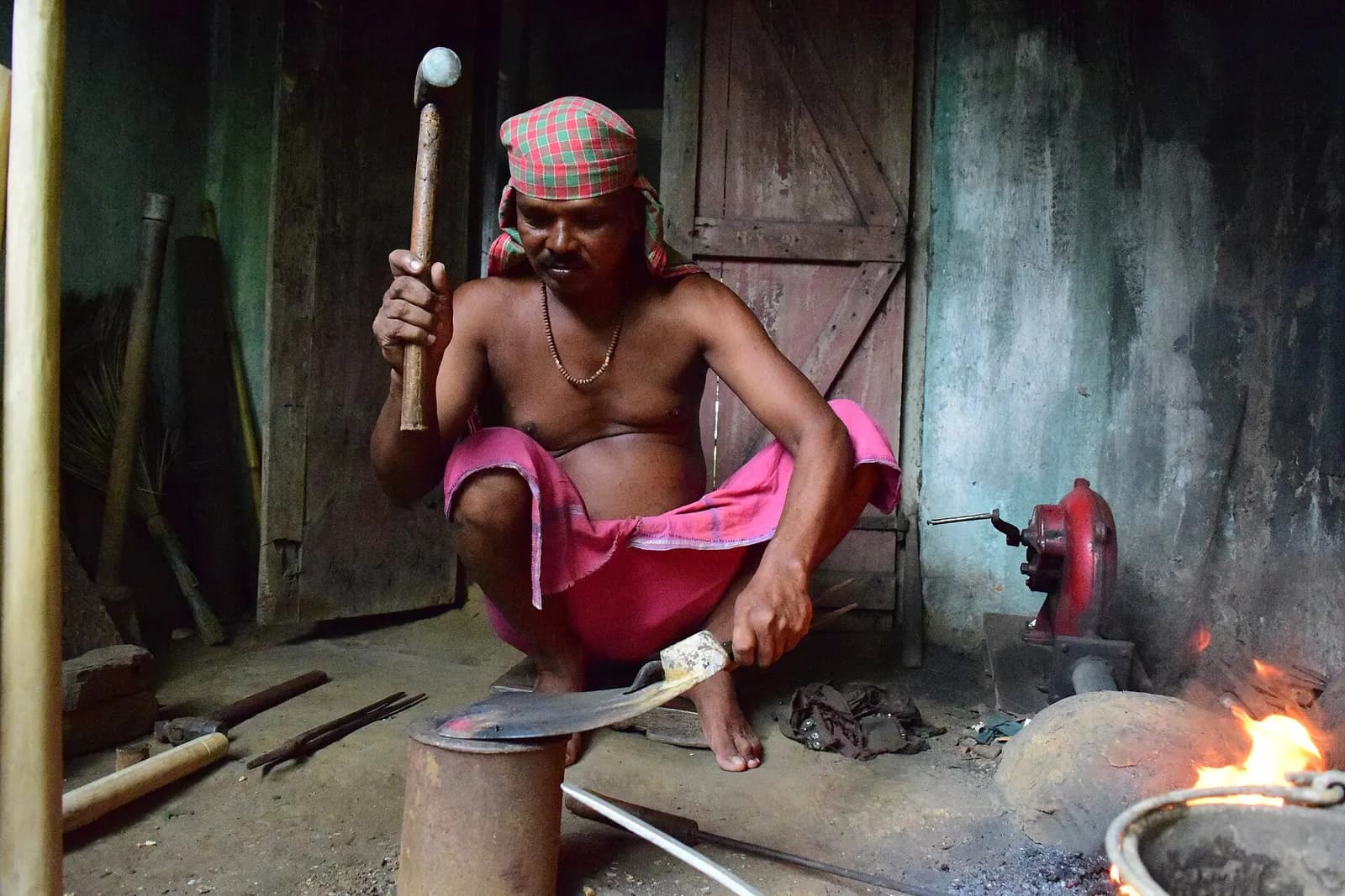 A blacksmith shaping a blade over a small forge in his workshop in Odisha