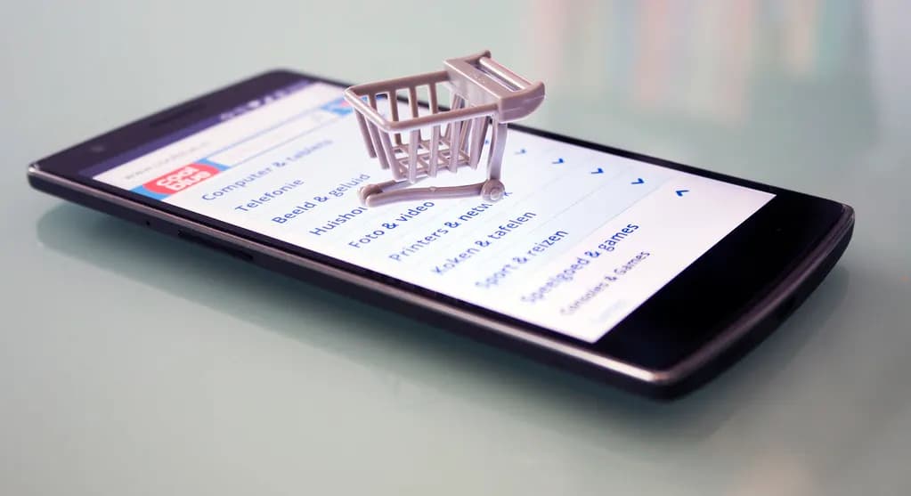 A smartphone showing an online shop's menu with a miniature shopping trolley placed on the screen