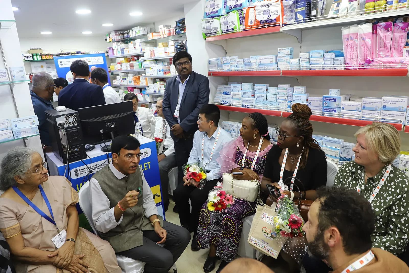 Inside an Indian pharmacy: medicine cartons on wall shelves, a billing computer at the counter and the pharmacist with visitors