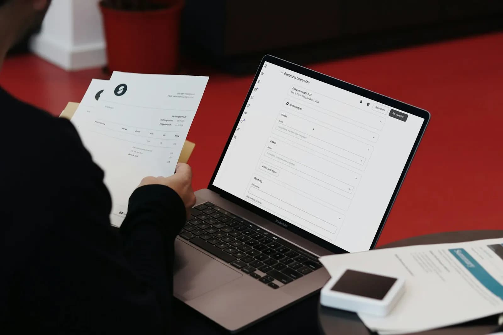 A person at a desk with a laptop and printed invoices, preparing B2B bills
