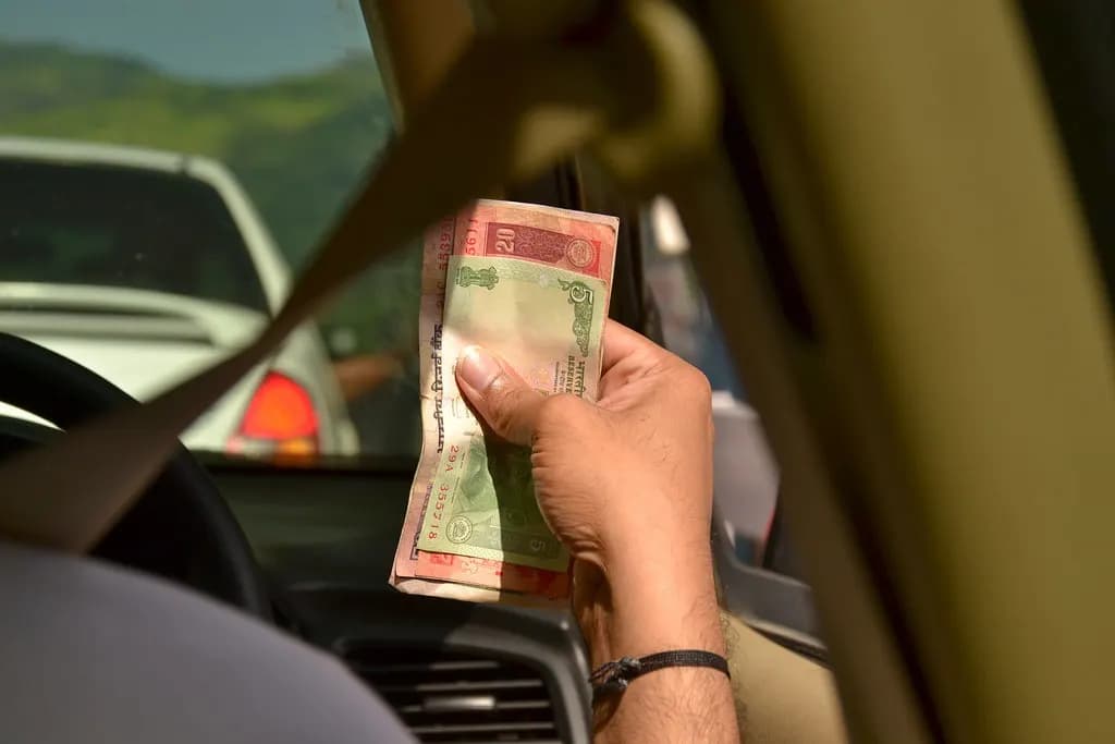 A hand holding a small bundle of Indian rupee notes inside a car