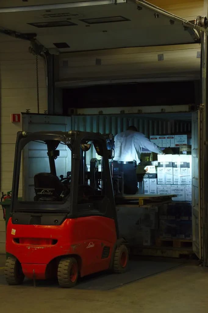 A forklift beside an open container being loaded with cartons of goods