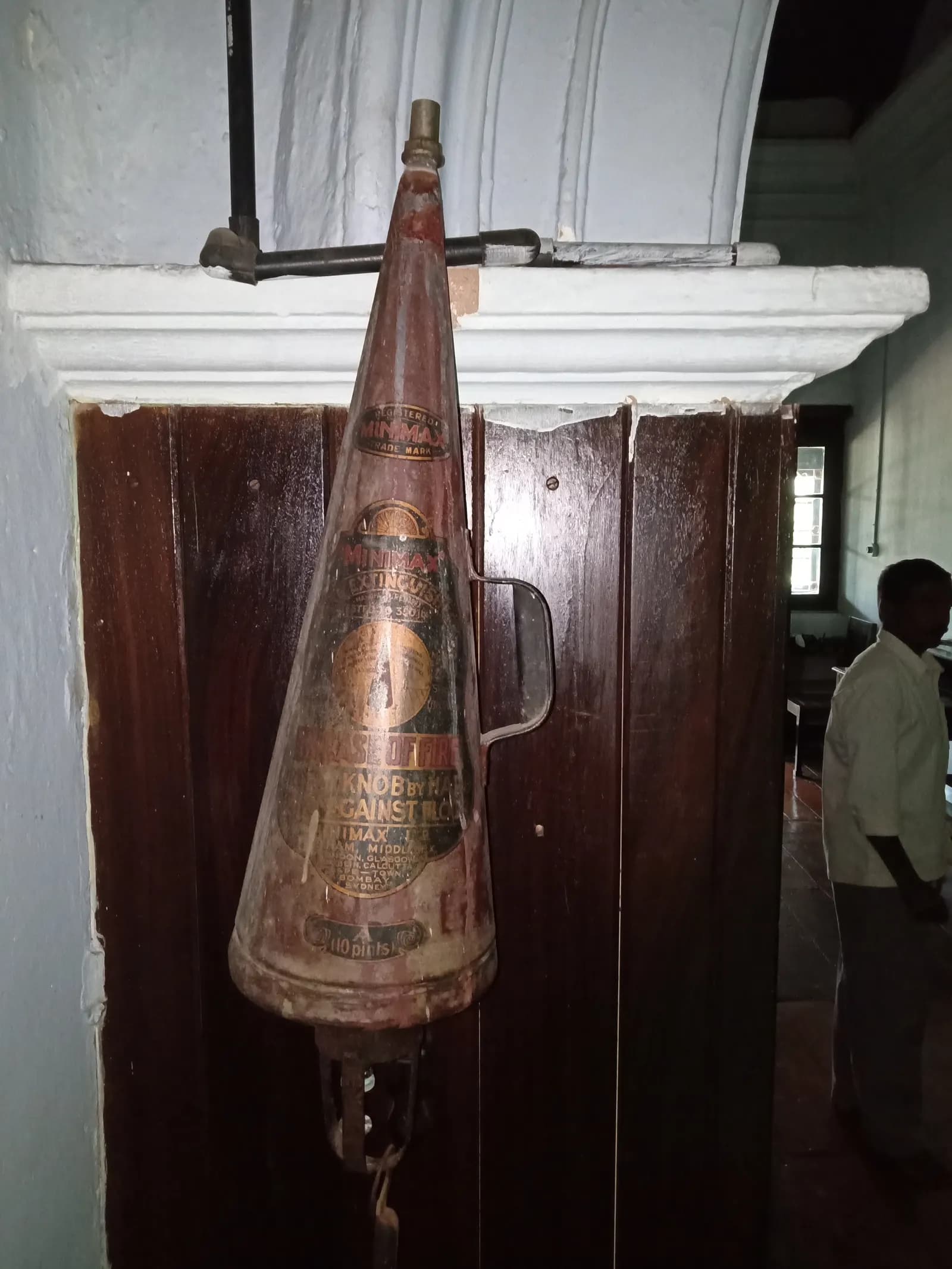 An old conical Minimax fire extinguisher hanging on a wooden wall panel