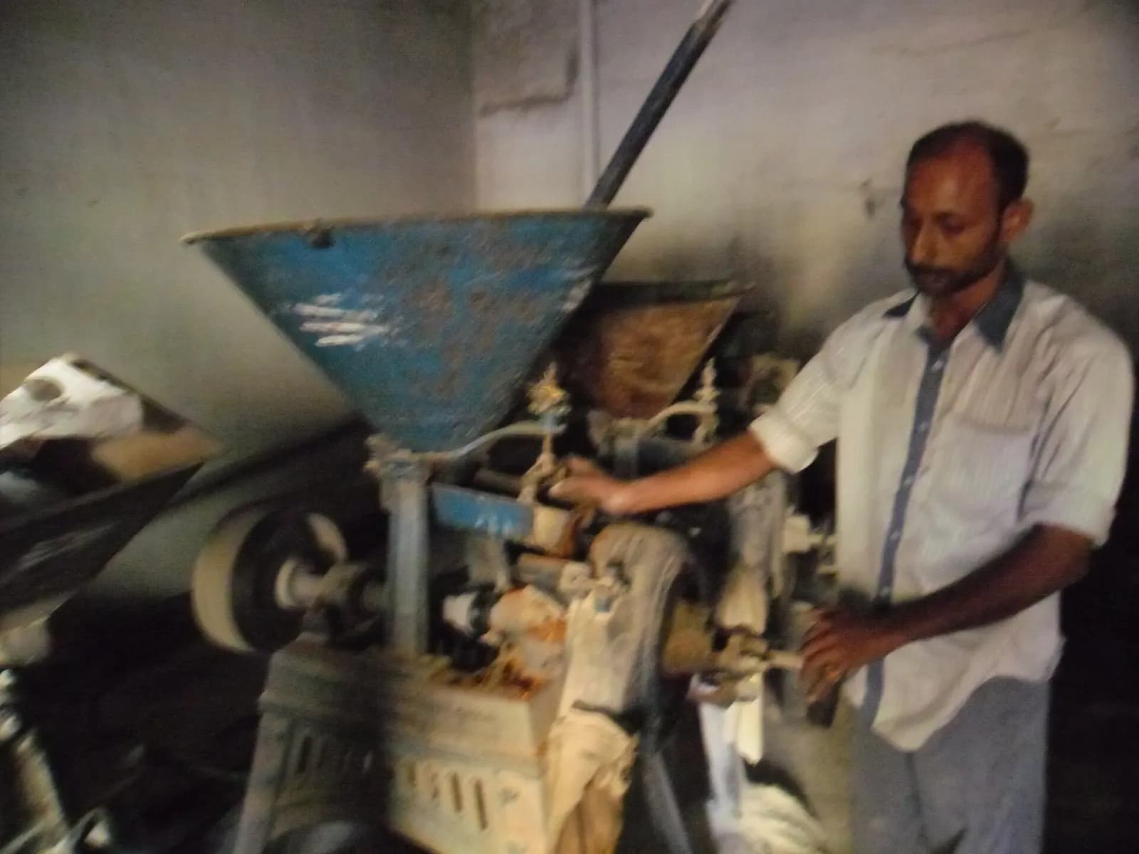 An operator adjusting a stone flour mill with a blue feed hopper in a small mill in Salem, Tamil Nadu
