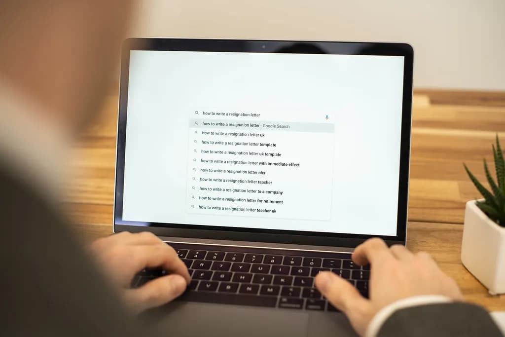 Someone typing a search on how to write a resignation letter on a laptop